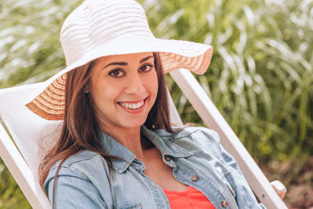 Smiling woman with hat relaxing on sunbed in the summer
