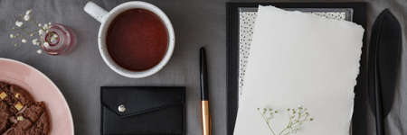 Top view of a lunch break arrangement with a cup of tea, pen and a piece of white paper mock-up on a table with gray fabricの写真素材