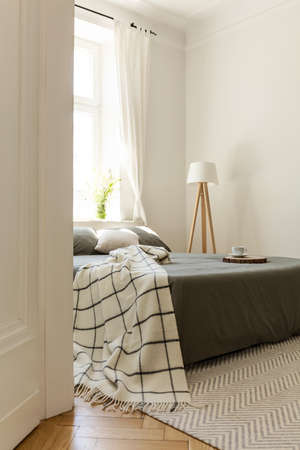 Flowers on the window next to bed in bright bedroom interior with khaki sheets. Real photo
