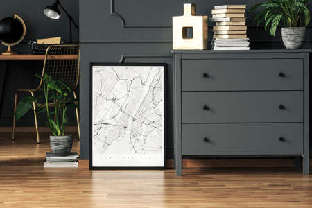 Map poster placed on the floor in real photo of dark grey room interior with fresh plants, gold decor and books on cupboardの写真素材