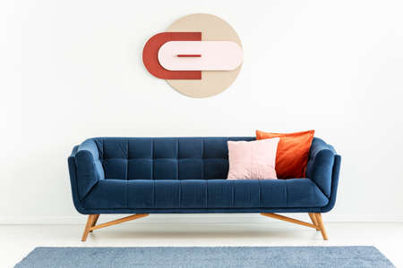 Pink and orange pillows on blue sofa in white apartment interior with poster and carpet. Real photoの写真素材