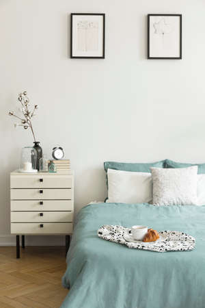 Real photo of white bedroom interior with breakfast placed on bed with pillows and pastel green...