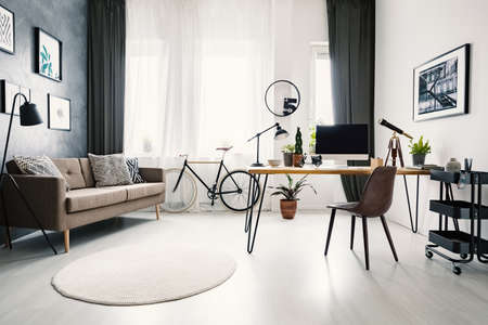 Modern home office interior with a big window, sofa, bike and desk with a computer. Real photoの写真素材