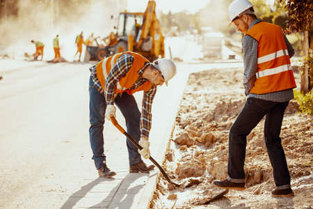 Workers in reflective vests using shovels during carriageway workの写真素材