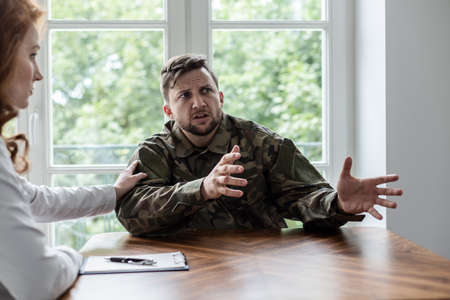 Soldier talking about his war experience with fear. Psychiatrist showing supportの写真素材