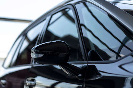 Close-up of a side mirror of a black family car for sale at a modern ...