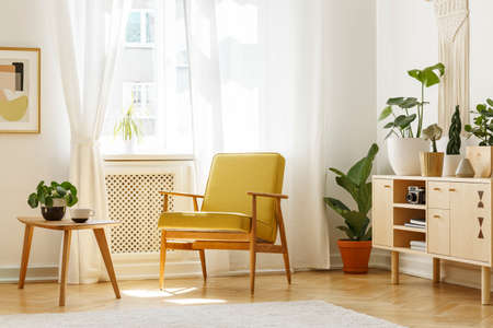 Real photo of a retro armchair, coffee table and cabinet in a living room interior decorated with...
