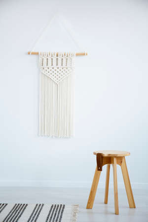 Wooden stool and rug in white simple living room interior with decor on the wall. Real photoの写真素材
