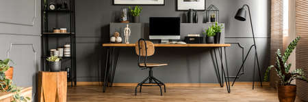 Wooden desk, fresh potted plants and mockup computer monitor standing in a dark grey living room interior with metal furnitureの写真素材