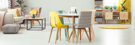 Yellow and grey chair at dining table in apartment interior with pouf next to sofa. Real photo
