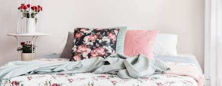 Panorama of floral pillow and blue blanket on bed in bright feminine bedroom interior. Real photo