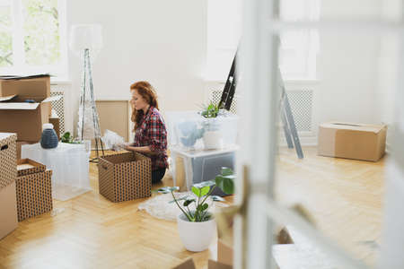 Woman unpacking stuff from carton boxes on the floor while moving-in