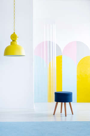 Real photo of an apartment interior with a large, yellow lamp and a simple, blue stool