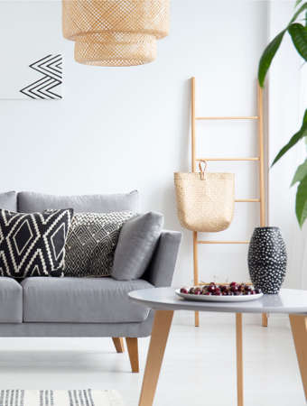 Patterned cushions on grey sofa under lamp in white flat interior with table and ladder. Real photoの写真素材