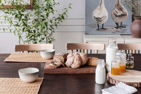 Milk, natural honey and bread on cottage wooden table in dining room interior with poster. Real photoの写真素材