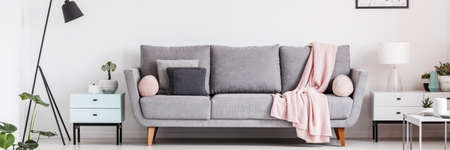 Grey lounge with cushions and pastel pink blanket in real photo of white living room interiorの写真素材