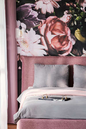 Grey cushions on pink bed in feminine bedroom interior with flowers wallpaper. Real photoの写真素材
