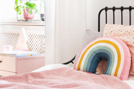 Pastel pillows on pink bed in girl's rainbow bedroom interior with white cabinet. Real photoの写真素材