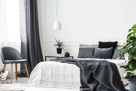 Natural light in a monochromatic bedroom interior with gray textiles, white wall, green plants and copy spaceの写真素材