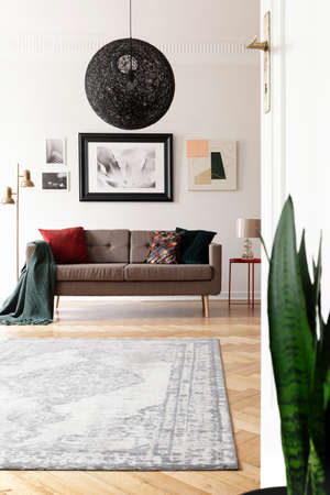 Low angle view of an artistic living room interior with a large, black, spherical pendant light above a brown sofa.の写真素材
