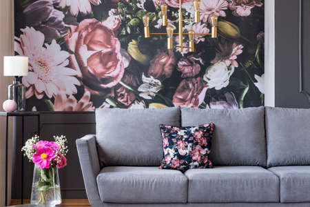 Real photo of a flower print behind a couch in a living room interior with fresh flowers in a vaseの写真素材