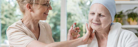 Panorama of friendly caregiver with perfumes supporting happy sick elderly womanの写真素材