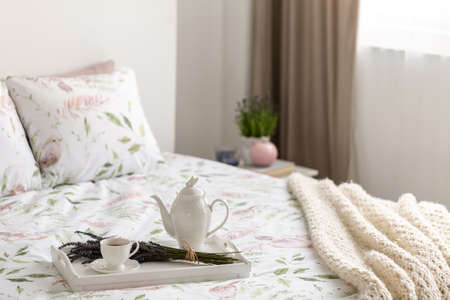 Tray on bed with pillows and blanket in hotel bedroom interior with lavender flowers on cabinet....