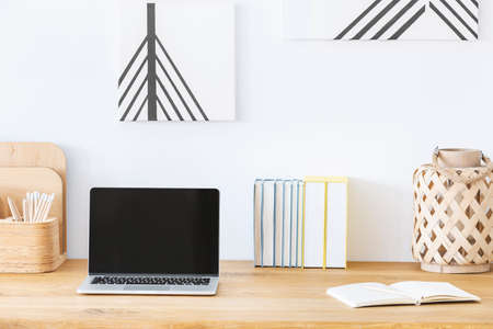 Close-up of a laptop on a desk next to a notebook and books in a home office interior. Empty screen,...