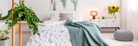 Close-up of a plant in a Scandinavian bedroom interior with a bed with patterned sheets, sunflowers...
