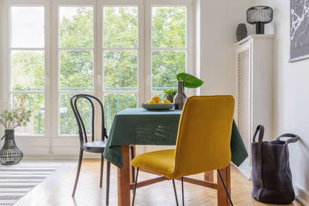 Real photo of a vintage dining room interior with a table, yellow chair and big balcony window