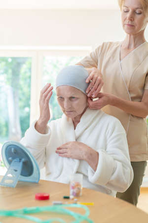 Caregiver helping senior woman with headscarf in the nursing houseの写真素材