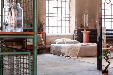 Knit blanket and cushions on bed in japanese bedroom interior with window and bonsai. Real photo