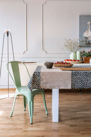 Green chair at table with food in grey dining room interior with lamp and wall with molding. Real...