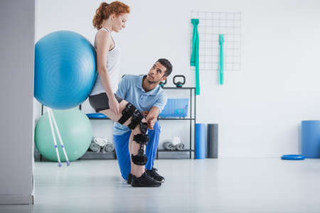 Woman with orthopedic problem exercising with ball while physiotherapist supporting herの写真素材