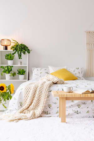 Sunny spring bedroom interior with green plants beside a bed dressed in eco cotton linen. Yellow...