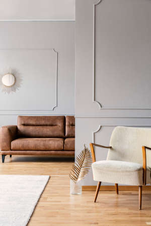 Vintage armchair in minimal living room of elegant apartment with brown leather sofa