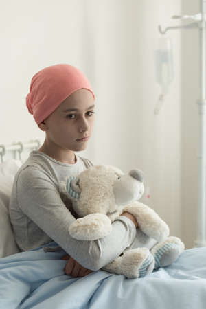Sad lonely sick girl with cancer hugging plush toy in the hospitalの写真素材