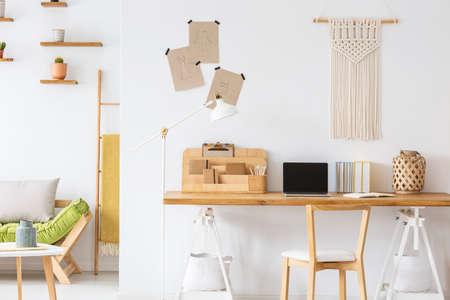 Wooden chair at desk with laptop and organizer in white home office interior with decor. Real photo