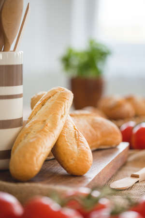 Close-up on baguette on wooden desk during breakfast with blurred tomatoes. Real photo