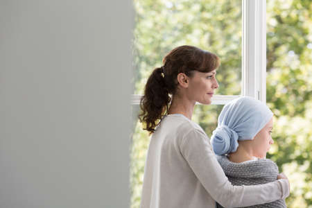 Mother and daughter with cancer in hospital, looking through the window in medical centerの写真素材