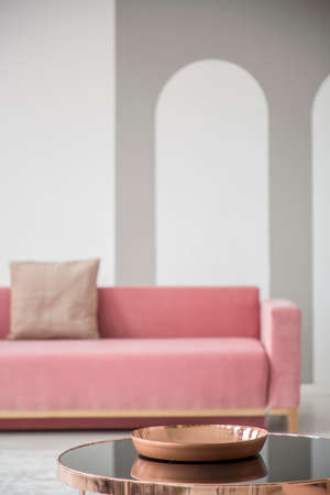 Focus on a golden rose bowl on a shiny black coffee table in an elegant living room interior with a pink sofaの写真素材