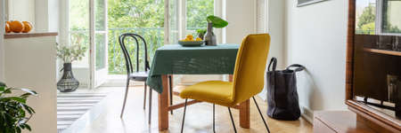 Panoramic view of stylish yellow chair next to table covered with green tablecloth in modern kitchen with balconyの写真素材