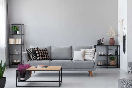 Copy space on the wall of scandinavian living room with modern couch, metal shelves and industrial coffee table, real photoの写真素材