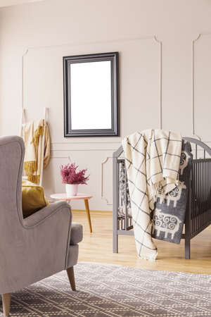 Mockup on the wall of mid century baby room with grey armchair, crib with blankets and heather in white pot on the tableの写真素材