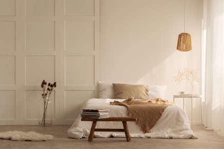 Beige blanket on the double bed in stylish wabi sabi bedroom of minimal style house, real photo with copy space on the empty wallの写真素材