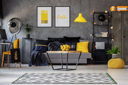 Lemons in metal basket on wooden coffee table in grey scandinavian living room with industrial furniture and patterned carpet, real photoの写真素材