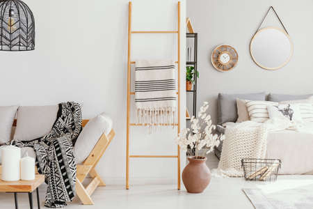 Wooden ladder with blanket between elegant settee with patterned blanket and comfortable bed with light grey bedding, real photoの写真素材