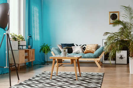 Blue curtains and wooden furniture in beautiful eclectic interior with comfortable sofa with pillows...