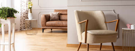 Panoramic view of retro armchair in elegant living room with brown leather sofa, real photo