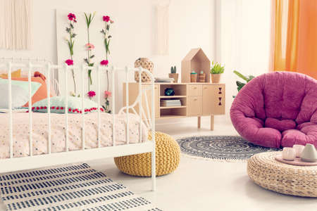 Stylish amaranth armchair in elegant girl's boho bedroom interior with flowers and wooden furnitureの写真素材